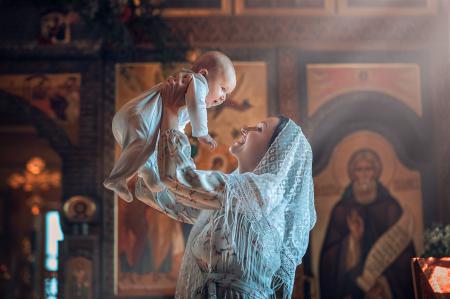 Счастливая женщина с ребенком на руках крестит младенца